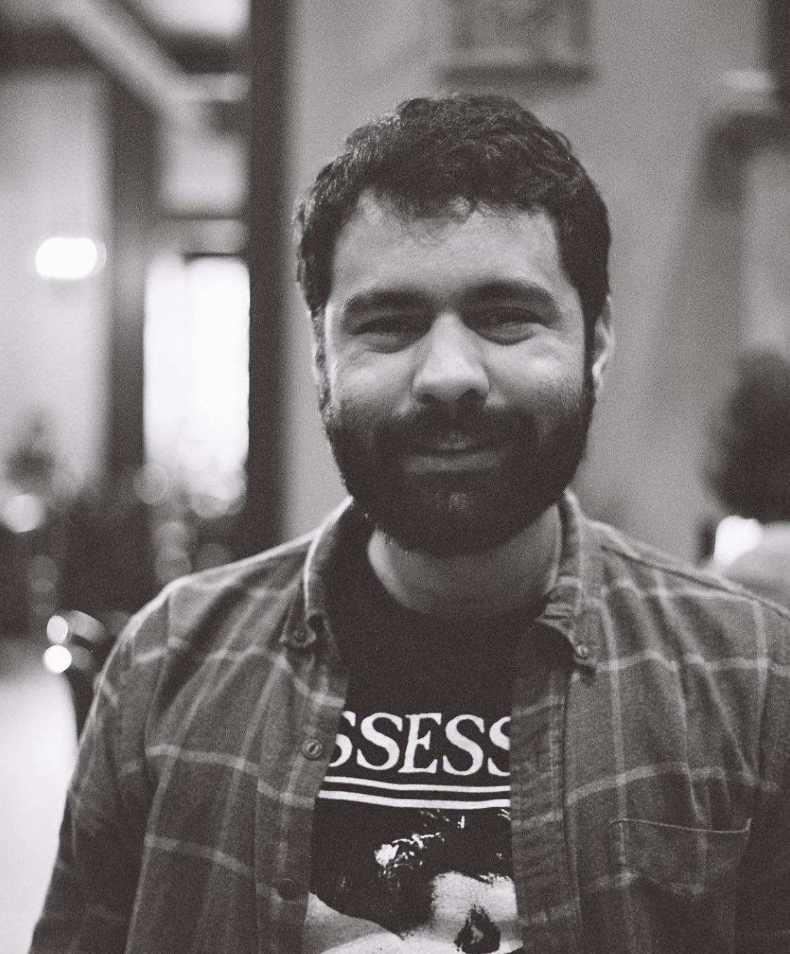 A black-and-white photo of a smiling bearded man with dark hair.